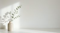 Minimalist eucalyptus branch in white ceramic vase on neutral surface with soft natural light and shadow, suitable for home decor and wellness design projects.