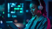 Young African American woman in headphones using smartphone at night, illuminated by vibrant neon pink and blue lights, creating modern urban atmosphere.