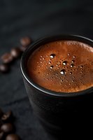 Rich espresso coffee with foam bubbles in black ceramic cup on dark slate background with scattered coffee beans for cafe menu design.