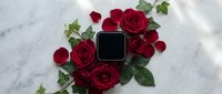 Elegant black square jewelry box surrounded by deep red roses and green ivy on a white marble surface, romantic luxury gift concept.