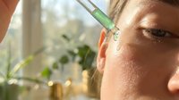 Young woman applying facial serum with dropper pipette in natural light skincare routine for healthy glowing skin anti-aging treatment at home.