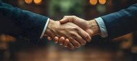 Close-up of firm business handshake between two men wearing suits against blurred warm background with bokeh lights, symbolizing trust and partnership agreement.