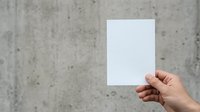 Hand holding blank white paper sheet against concrete wall background for mockup and branding purposes.