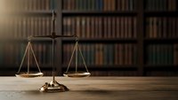 Brass scales of justice on wooden desk with law books in background for legal office and courtroom concepts.
