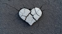 Cracked heart shape on dark concrete surface showing broken love concept, relationship problems and emotional pain. Suitable for relationship counseling materials.