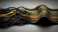 Colorful woven textile with flowing wave pattern displaying vibrant threads in rainbow spectrum creating dynamic undulating surface for fabric design projects.