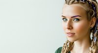 Young Caucasian woman with braided hairstyle and decorative beads, wearing green top, looking at camera with neutral expression against white background for portrait and beauty use.