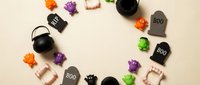 Halloween party decorations arranged in circle frame with mini pumpkins, cauldrons, tombstones and spooky elements on beige background for festive design.