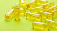 Yellow gel capsules scattered on bright green surface for health and wellness supplement marketing materials.