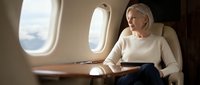 Elegant blonde businesswoman in white sweater working on laptop during luxury private jet flight with scenic window view.