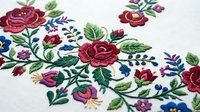 Traditional folk embroidery with colorful floral motifs featuring roses and leaves on white fabric. Handcrafted textile art for cultural projects and decor.