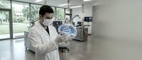 Male dentist in white coat and protective mask examining dental X-ray in modern clinic office with large windows and professional equipment.