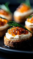 Gourmet appetizer with red caviar, cream cheese and fresh rosemary on toasted bread round, served on dark plate. Close up view with selective focus.