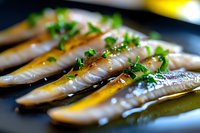 Fresh mackerel fillets garnished with chopped chives and olive oil on black plate, close-up view showing raw fish texture and natural sheen in restaurant setting.