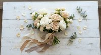 Elegant bridal bouquet with cream roses and eucalyptus leaves tied with silk ribbon on rustic white wooden background for wedding celebration.