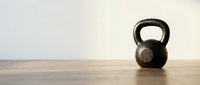 Black kettlebell weight on wooden floor against white background, isolated for fitness, gym training, strength workout, and exercise design projects.