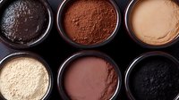 Different shades of cocoa powder and chocolate ingredients in round bowls arranged on dark background, top view for food photography and confectionery design.