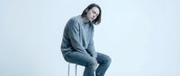 Young Caucasian man in casual blue sweatsuit sitting on modern chair against white background, relaxed pose for lifestyle and fashion content.