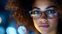 Young mixed race woman with curly hair and glasses in night city lights, glowing bokeh circles create dreamy atmosphere. Professional portrait with blue tones.