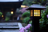 Traditional Japanese garden lantern glowing at dusk with pink azalea flowers and stone path, creating serene atmosphere for meditation and zen gardens.