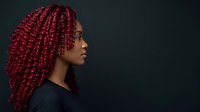 Young woman with deep burgundy braided hair, African descent, wearing black clothing against dark background, side profile portrait for beauty and fashion concepts.