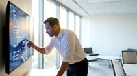 Professional businessman using interactive touchscreen display in modern office conference room for data analysis and business presentation.