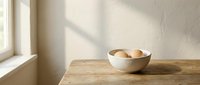 Minimalist kitchen scene with fresh eggs in ceramic bowl on rustic wooden table near window with natural sunlight creating soft shadows on textured wall.