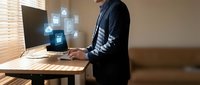 Professional businessman using laptop with holographic digital security icons in modern office workspace for cybersecurity and data protection concepts.