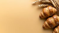 Fresh baked croissants and golden wheat ears on beige background with copy space. Minimal food composition for bakery or breakfast concept.