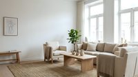 Bright minimalist living room with neutral beige sofa, wooden furniture, potted plant, and natural light from large windows, suitable for interior design and home decor projects.