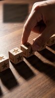Hand placing wooden blocks with star ratings on table for customer feedback and quality assessment in business evaluation process.