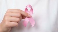 Female hand holding pink ribbon symbol for breast cancer awareness campaign against white medical coat background for healthcare support.