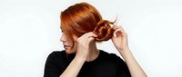 Young woman with copper-red hair styling her braid against white background. Suitable for beauty, hair care, and lifestyle content.