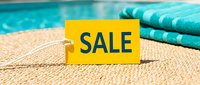 Yellow sale tag on poolside surface with turquoise towel and water in background, summer discount shopping concept.