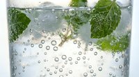 Refreshing sparkling water with fresh mint leaves and ice cubes in clear glass. Carbonated beverage with bubbles for summer drinks and healthy hydration concepts.