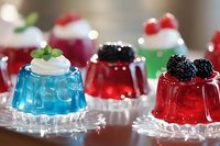 Colorful jello desserts topped with whipped cream, fresh berries and mint leaves on crystal plates, perfect for party buffet or holiday celebration.