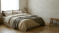 Cozy bedroom interior with unmade bed featuring neutral striped bedding, wooden furniture, and natural light from window for home decor design.