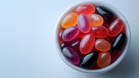 Colorful jelly beans in white ceramic bowl on light background. Assorted fruit flavored candies with glossy surface showing sugar crystals and vibrant colors.