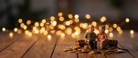Miniature elderly couple figurines sitting on wooden surface with warm golden bokeh lights creating romantic atmosphere for holiday decorations and storytelling.