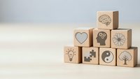 Wooden blocks with mental health and wellness symbols including brain, heart, lightbulb, and yin yang arranged on neutral background for mindfulness concepts.