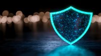 Glowing turquoise shield symbol with sparkles floating above reflective dark surface against blurred bokeh background represents digital security and protection.