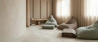 Minimalist modern living room interior with sage green bean bag chairs, wooden desk, and neutral beige tones creating serene contemporary home decor.
