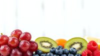 Fresh mixed fruits border with red grapes, kiwi slices, orange, blueberries and strawberry on white background for healthy eating and nutrition concepts.