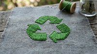 Green recycling symbol embroidered with yarn on rustic burlap fabric, promoting sustainable living and eco-friendly textile crafts.