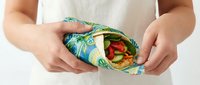 Eco-friendly reusable food wrap with tropical leaf pattern holding fresh sandwich, sustainable zero waste kitchen alternative to plastic wrap.