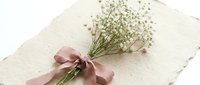 Delicate gypsophila bouquet tied with a dusty rose ribbon resting on textured handmade paper, soft romantic styling for wedding stationery.