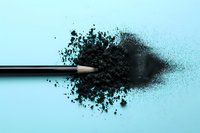 Black pencil with scattered charcoal powder creating artistic splash effect against light blue background, minimalist composition for creative and artistic concepts.