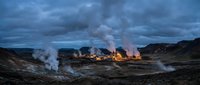 Geothermal power plant with steam rising from industrial facility against dramatic cloudy sky in volcanic landscape during twilight hours for energy concepts.