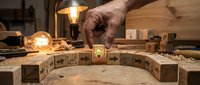 Craftsman hand placing wooden blocks with intricate carved symbols in warm workshop lighting. Traditional woodworking and handmade craftsmanship concept.