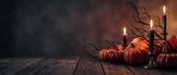 Autumn Halloween scene with orange pumpkins and burning candles on rustic wooden table against dark moody background for seasonal decorating.